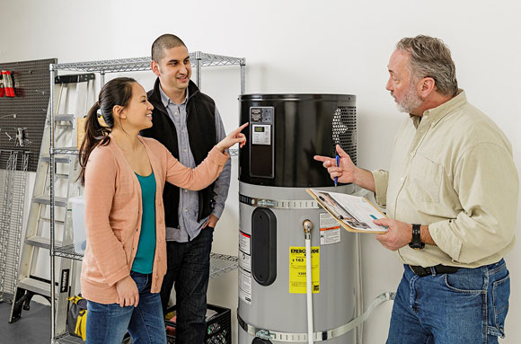 Three people talking standing near a water heater.