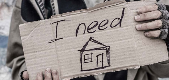 person holing a sign that reads "I need housing."