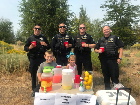 City of Bend Police officers drinking lemonade in front of kids' lemonade stand.