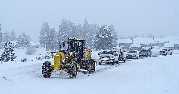 Cars trailing a grader plowing snow.