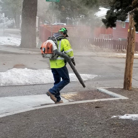 Streets department worker cleaning accumulated dirt from curb ramp.