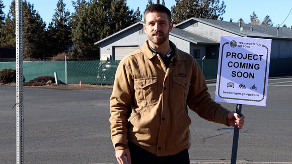 City Engineer standing on the side of a road holding a sign that reads: "Project coming soon"