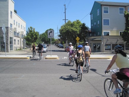 A group of people riding bicycles in the street with a traffic island.