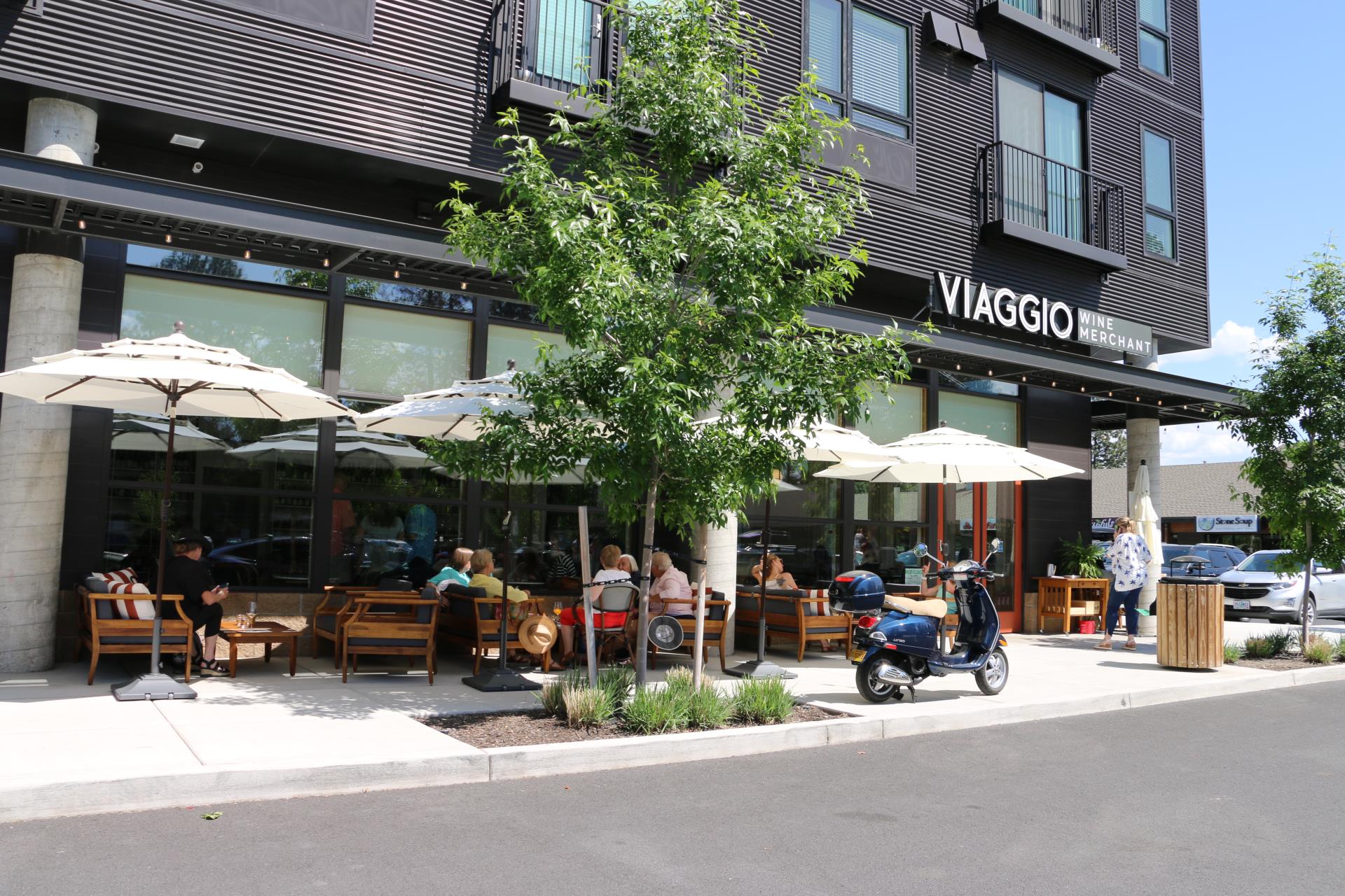 Image of people sitting outside of a wine bar located on the ground floor of a multiple unit residential building.