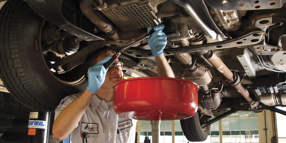 Mechanic draining oil into pan under a car