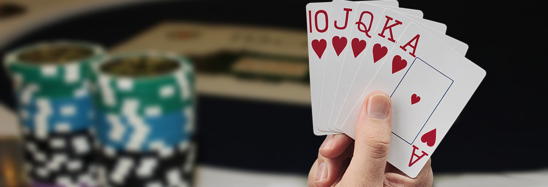 Hand holding four playing cards all Aces, poker chips blurred in the background