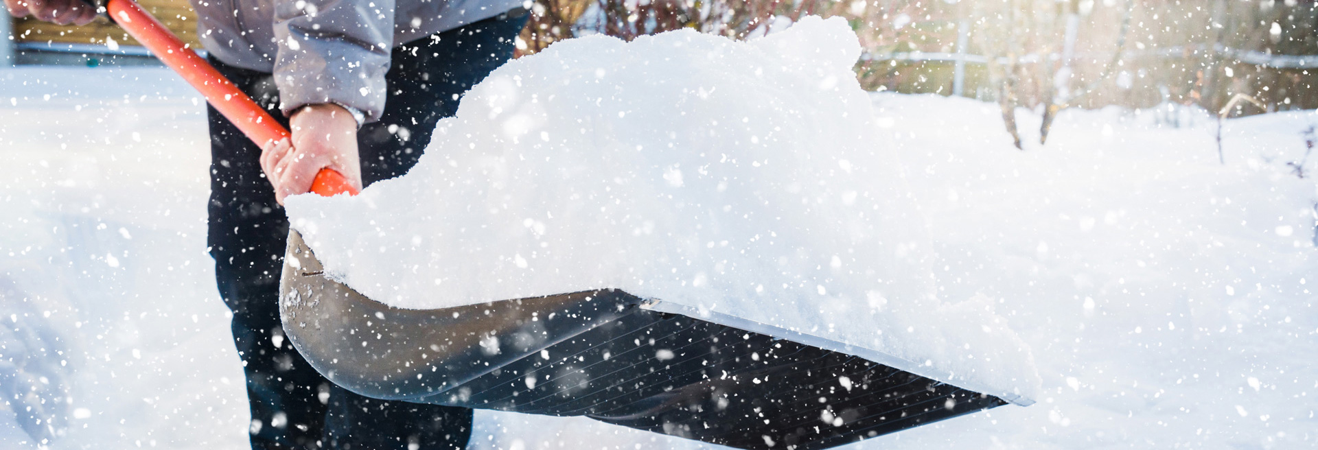 Person using a snow shovel to remove snow from a sidewalk