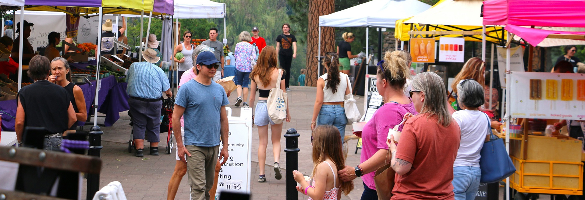 Event on a street with diverse people walking and looking at booths of goods for sale.