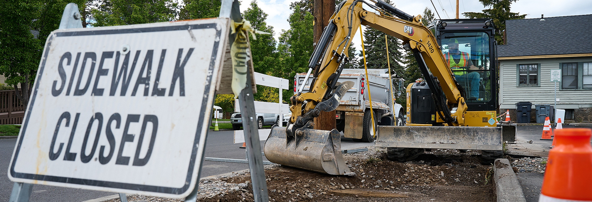 Sidewalk closed sign over an open sidewalk with an excavator working on the sidewalk