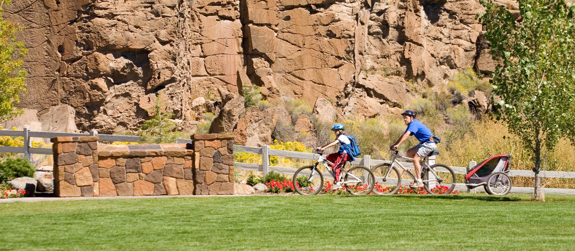 Family biking through park with rocky cliff in the background.