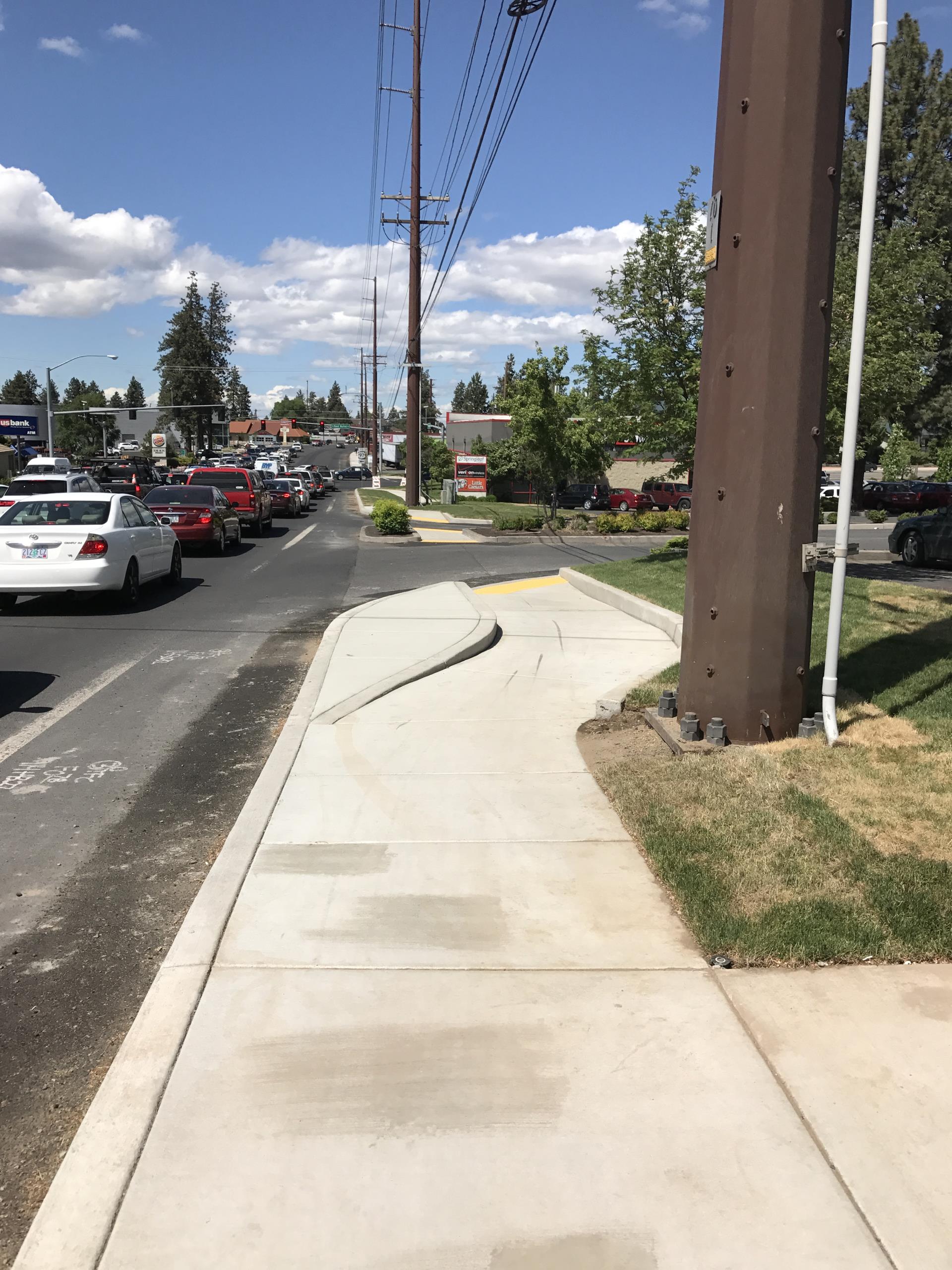 Completed sidewalk including ADA ramp and traffic driving by on the left