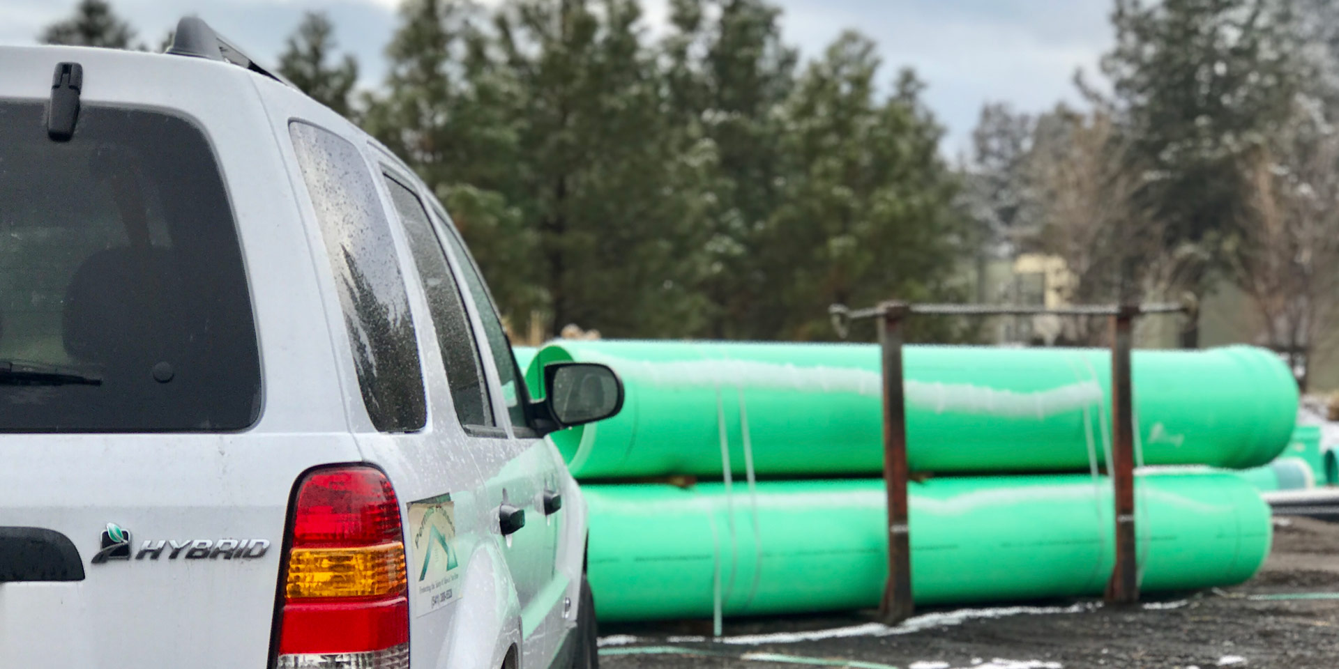 City hybrid vehicle parked in front of sewer pipes ready to be installed.