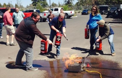 Four people using fire extinguishers in fire extinguisher training with live fire.