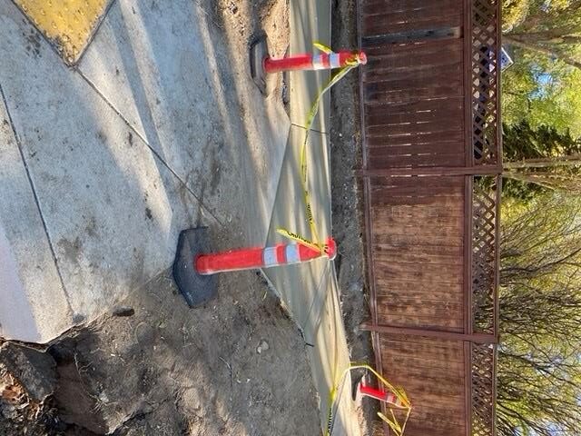 A photo of a section of newly poured sidewalk, surrounded by cones and caution tape.