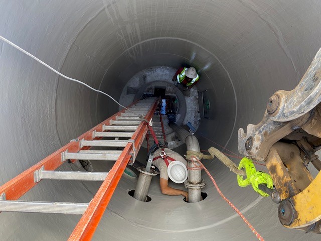 A photo looking down into a new manhole as work crews use ladders and a safety harness to install pipe for new pumps.