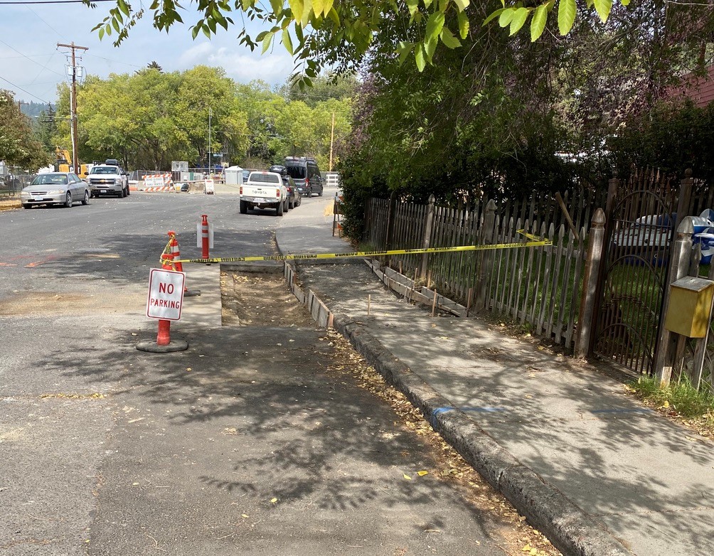 A photo of an ADA ramp under construction and surrounded with caution tape, cones, and no parking signs.