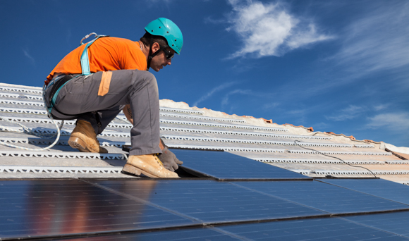 Man in safety equipment installing solar panels on a roof.