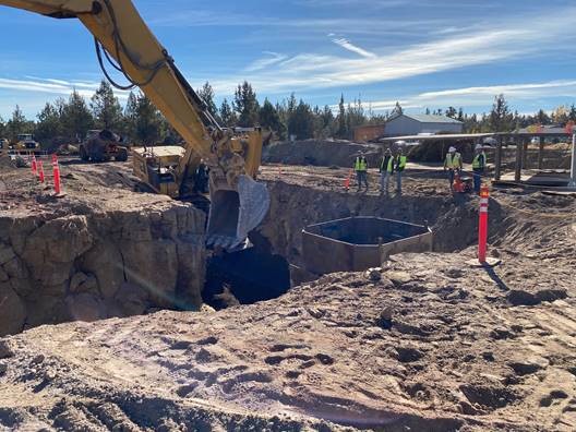 A photo of work crews working next to a trench while excavation equipment is being used for pipe installation work.