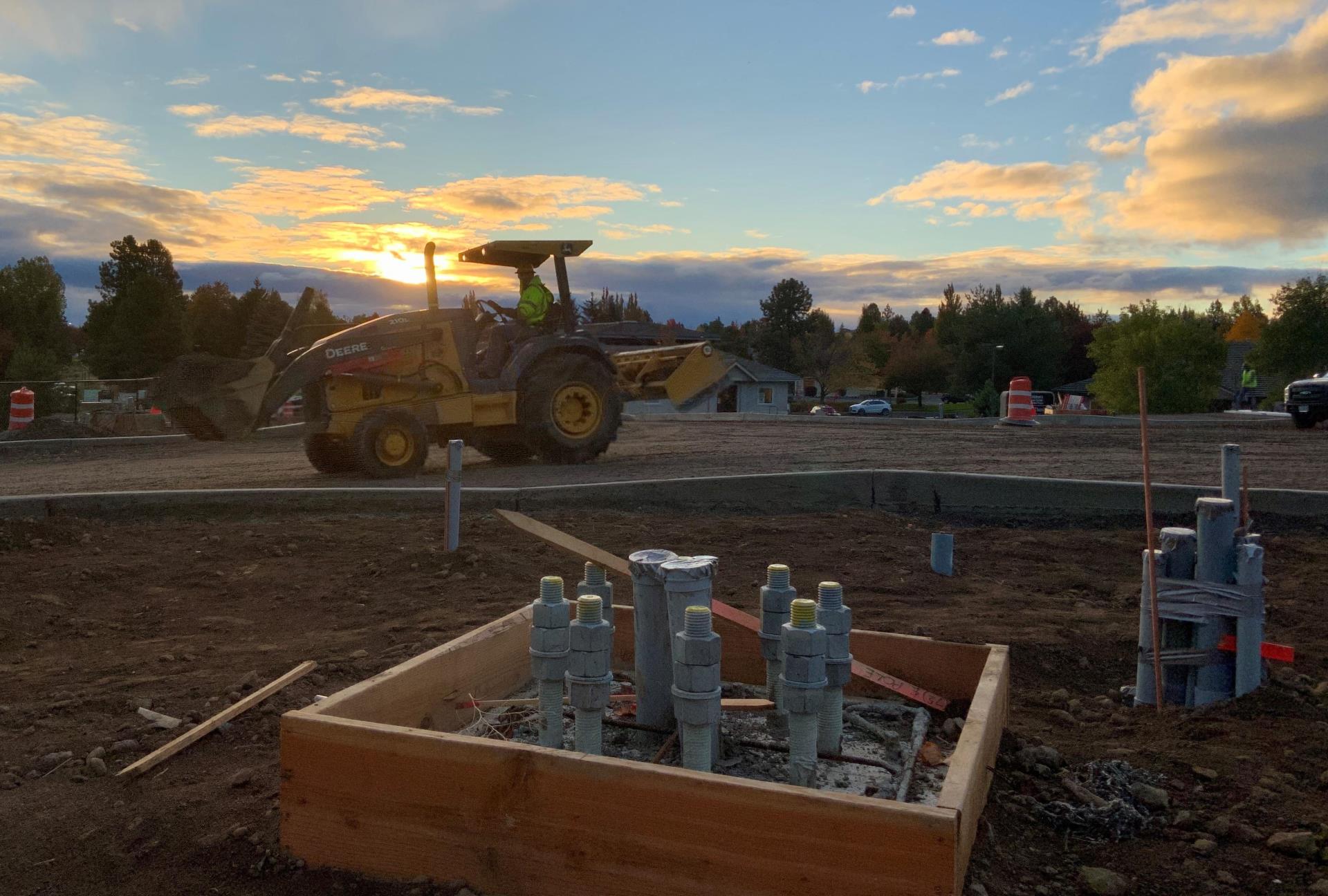 Electrical components installed for traffic signal pole. Loader hauling fill material at sunrise.