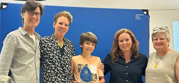 A picture of several people and a middle school student holding a trophy