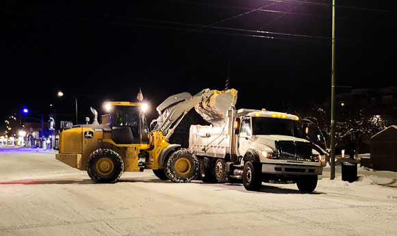 Excavator machine dumping snow into dump truck at night