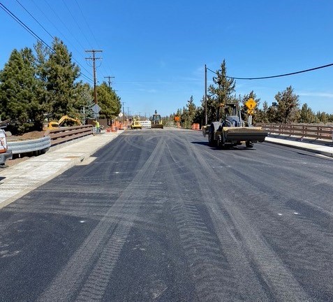 A photo of work crews and construction equipment working on the widening of the Purcell Bridge over the North Unit Irrigation District canal. The bridge has sidewalks and is paved.