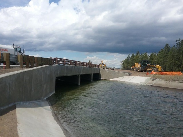 A photo of the Empire crossing structure with irrigation water flowing in the canal under it and construction equipment in the background.