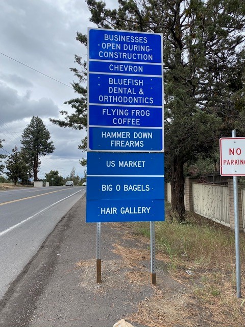 A picture of a blue road sign displaying seven businesses open during construction at the intersection of 27th Street and Butler Market Road.