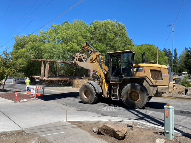 Work crews using heavy construction equipment to move a large metal part on NW Riverside Blvd.