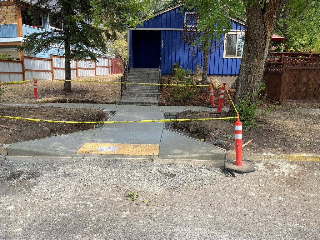 A photo of cones and caution tape surrounding a new ADA ramp and sidewalk.