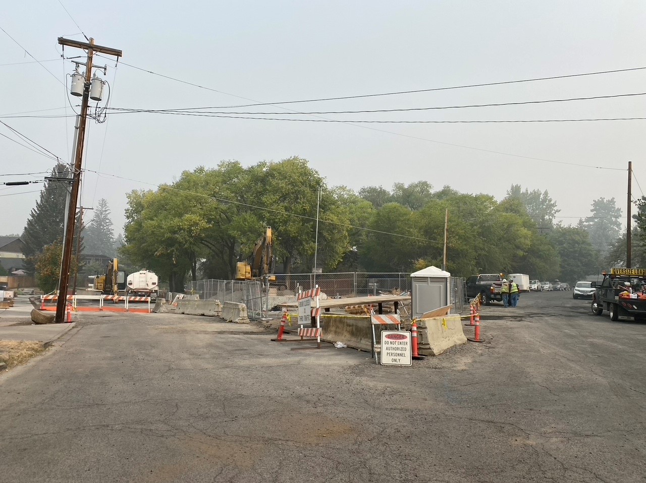 A photo of work crews and equipment at NW Riverside Blvd & NW Congress St. Fencing, barricades, caution tape, and cones surround the job site and NW Riverside Blvd closure.