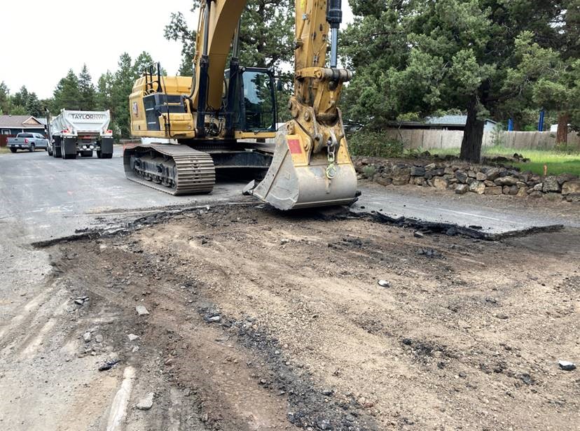 A photo of work crews using an excavator to remove asphalt in preparation for rock-hammering and trench excavation.