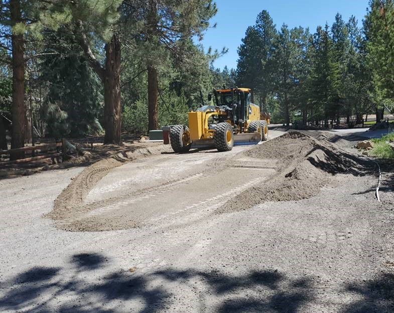A photo of work crews using a motor grader to perform road base grading in preparation for paving on King Hezekiah Way.