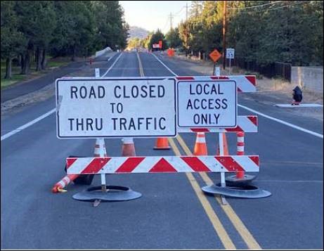 A photo a barricade, cones, and road signs marking the road closure to thru traffic and local access only.