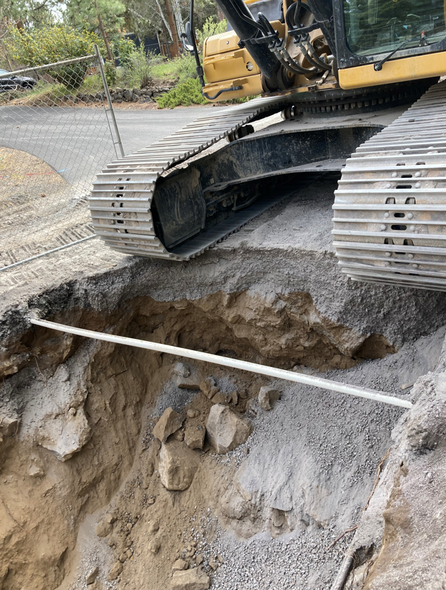 A photo of an exposed utility conduit crossing in an open sewer trench in front of an excavator.