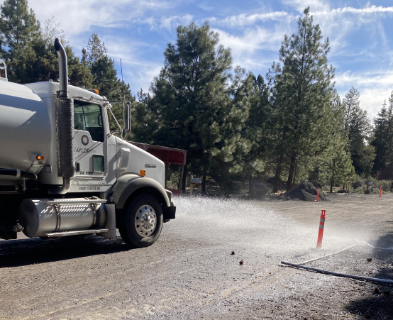 A photo of a water truck spraying water on the unpaved roadway to ensure dust is kept to a minimum during construction.