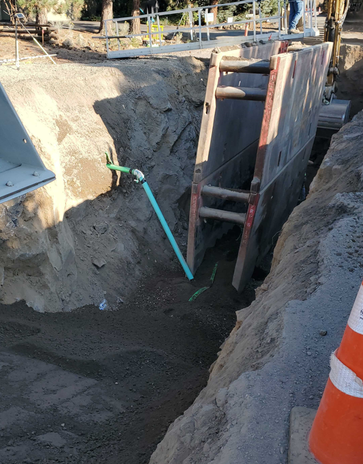 A photo of the sewer trench. In the trench is a trench wall and a sewer lateral pipe coming from the property line and dropping into the sewer main pipe.