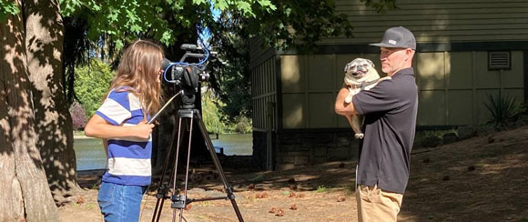 a young girl filming a man holding a  dog.