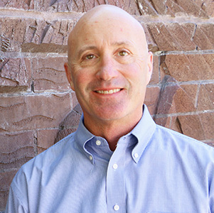 Colin is light skinned and is wearing a light blue button down shirt.