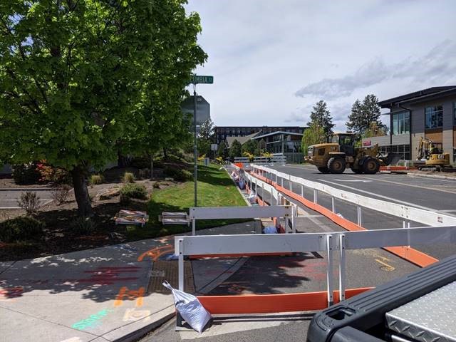 A photo of temporary pedestrian paths being installed along Simpson Ave. There is a barricade road closure and large construction equipment in the background.