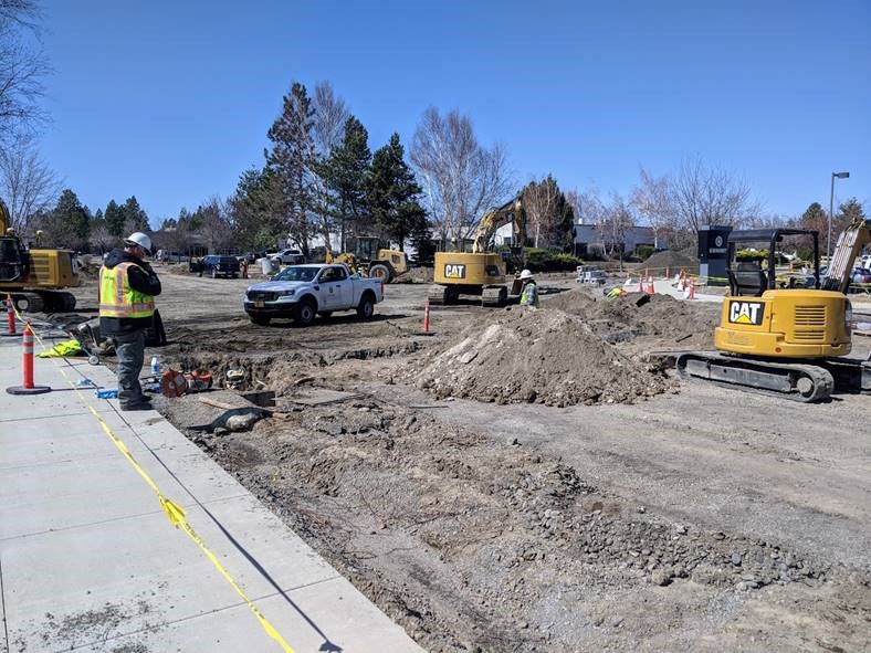 A photo of the work crew testing the newly relocated waterlines. Cones and yellow tape surround the project perimeter. There is equipment and mounds of earth from the waterline trench excavation at the project site.