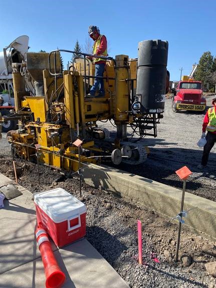 A photo of work crew members using equipment to pour concrete curbs.