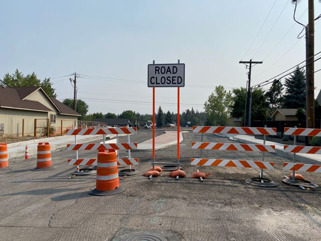 A photo of NE Purcell Blvd and NE Butler Market Road facing south. There are cones, barricades, and a ROAD CLOSED street sign closing the street during construction of the roundabout.