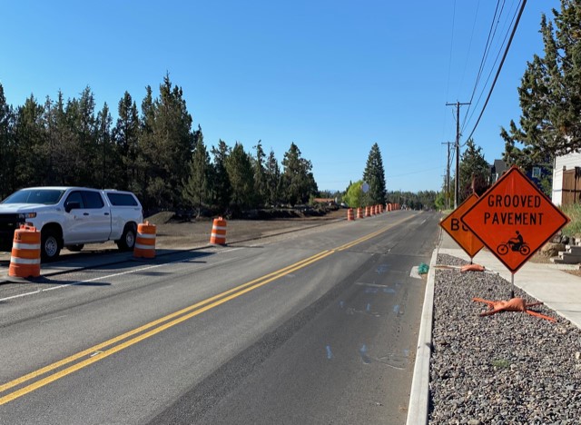A photo of the grooved and graveled road and a transition bump in the pavement on Purcell Blvd. There are cones, a BUMP sign, and a GROOVED PAVEMENT sign on the shoulder of the road.