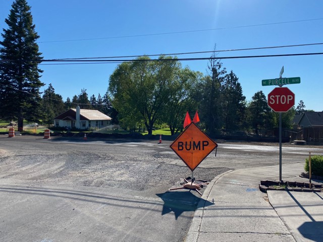 A photo of the uneven road and graveled surface at the NE Purser Ln. & Purcell Blvd. intersection. There is a BUMP sign and cones along the shoulder of the road.
