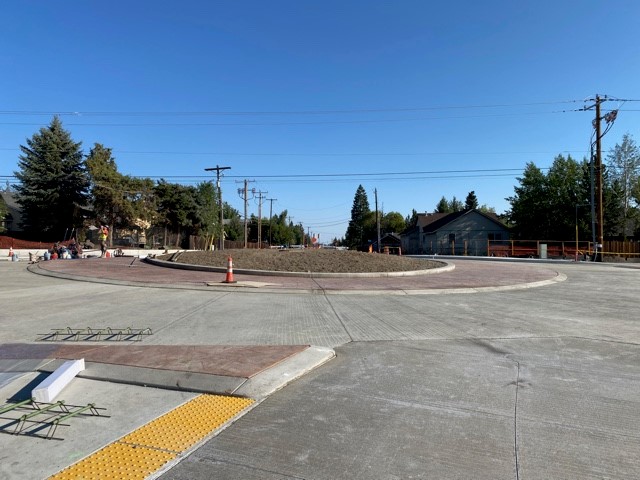 A photo of NE Butler Market Road facing east. There are cones, yellow caution tape, barricades, and road signs surrounding the project site and marking the road closure.