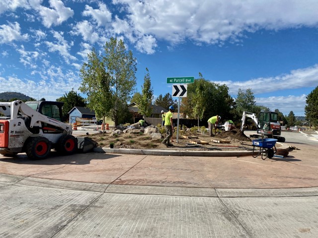 A photo facing west at the new NE Purcell Blvd & NE Butler Market Rd roundabout. A work crew is landscaping the center of the roundabout.