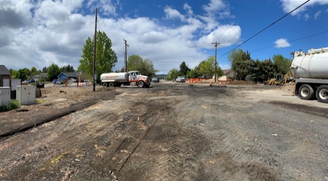 A photo of Butler Market Road facing west near NE Purcell Blvd. There are barricades, cones, tank trucks, and a backhoe excavator at the project site.