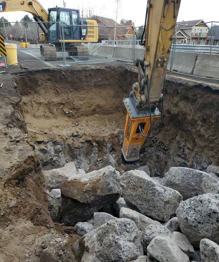 A photo of large equipment excavating in a trench with a rock hammer west of the COID canal bridge.