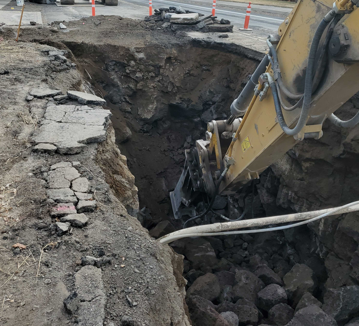 A photo of large equipment excavating in a trench with a rock hammer.